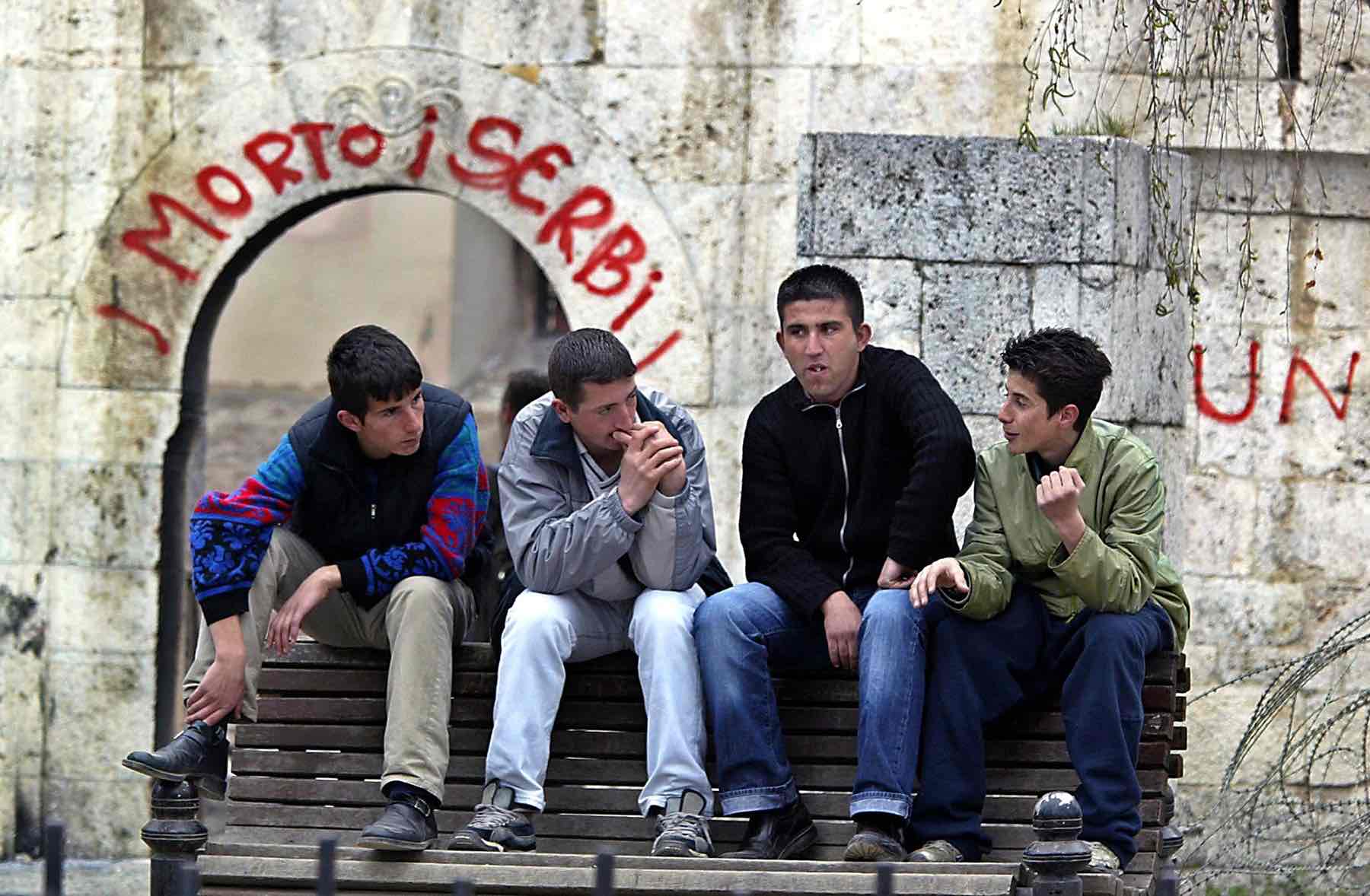 Albanian youths chat in front of a destroyed church in Prizren